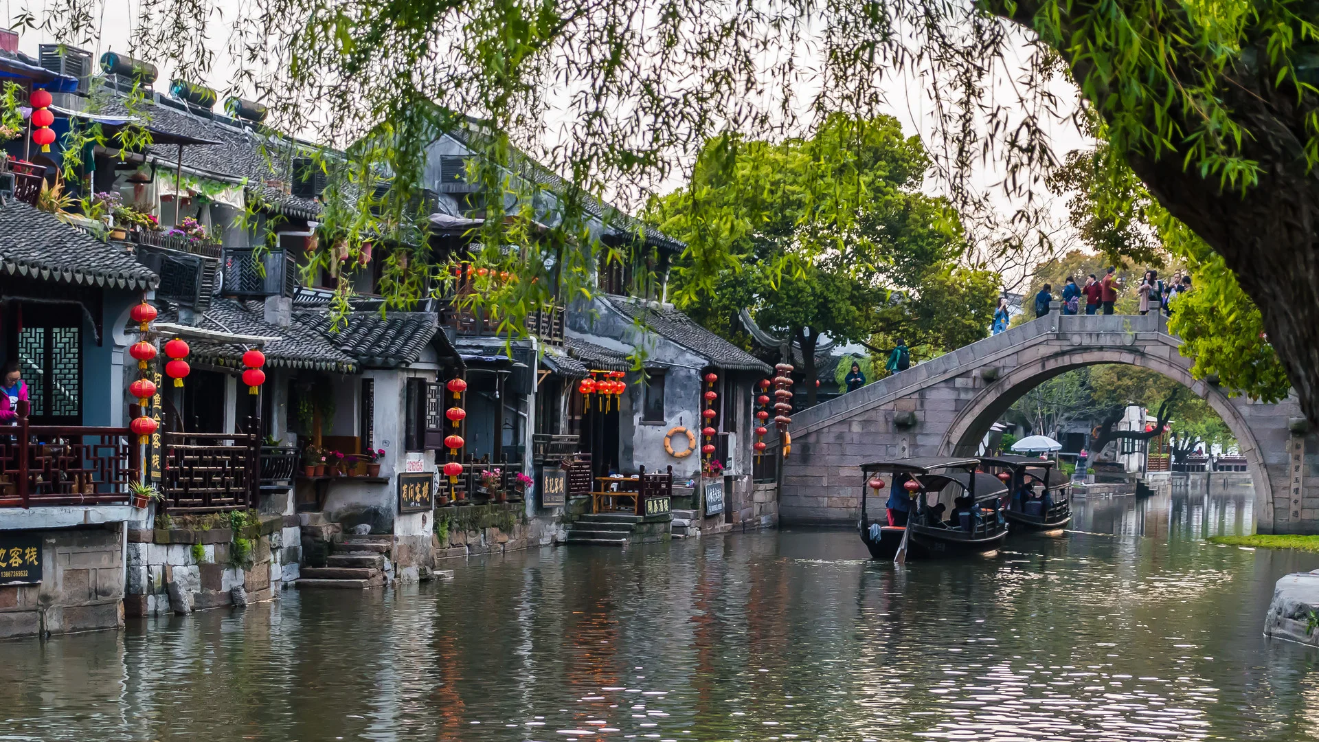 Serene Jiangnan river landscape with old stone bridge, canal boats, and whitewashed village houses