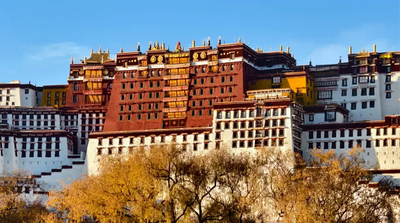 Ancient Tibetan temple courtyard with monks, red walls, and golden roof details